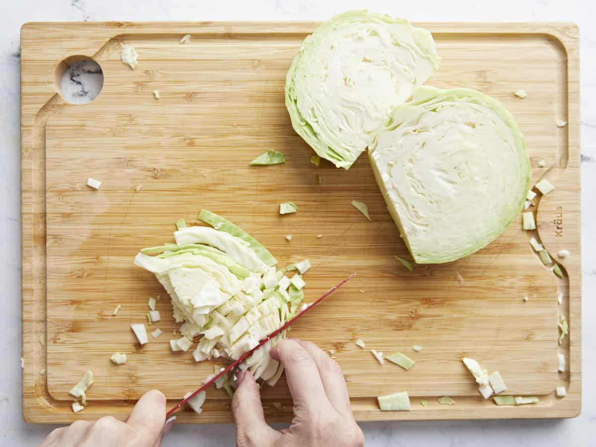 Overhead shot of green cabbage being sliced on a cutting board.
