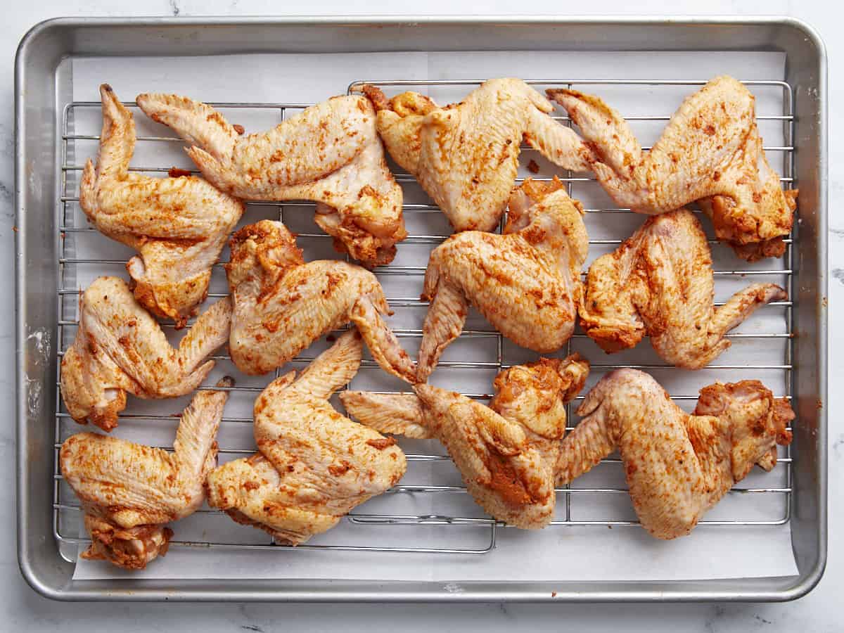 Overhead shot of seasoned and sauced chicken wings set on a rack in a sheet pan.