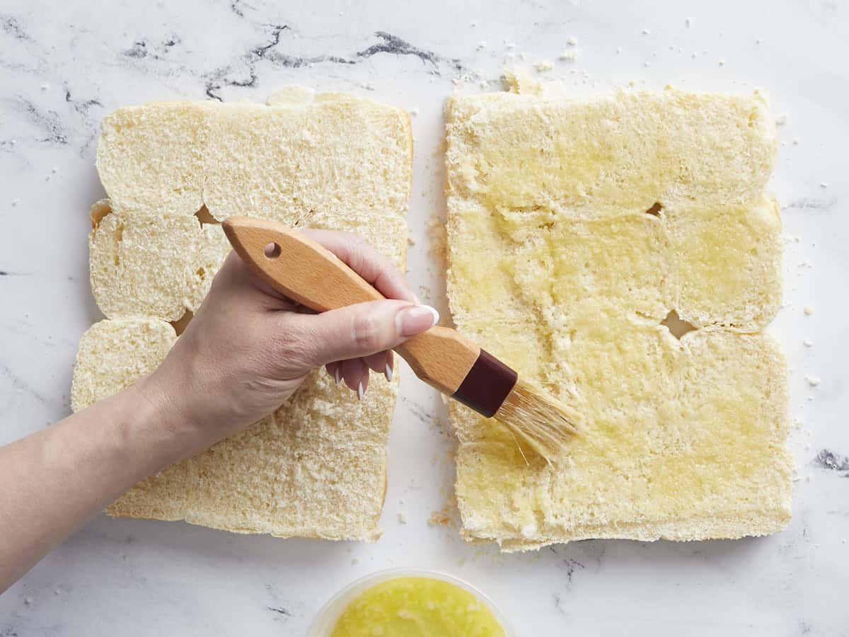 Hawaiian rolls cut in half being brushed with butter.