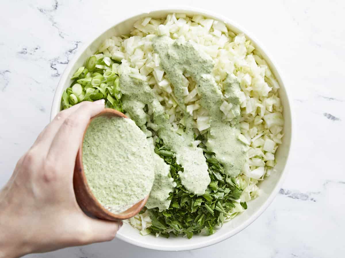 Overhead shot of Green Goddess Dressing being added to chopped greens in a white bowl.