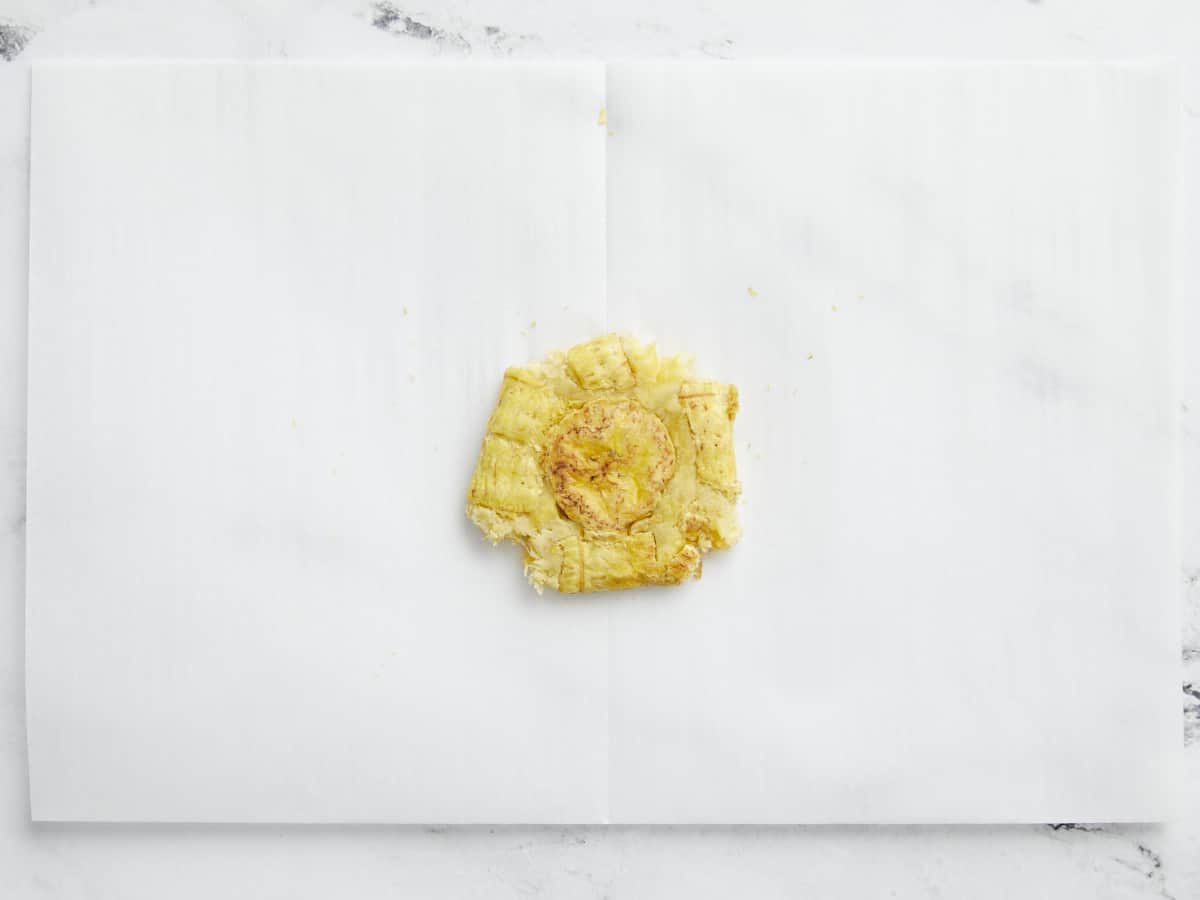 Overhead shot of smashed green plantain on white parchment paper.