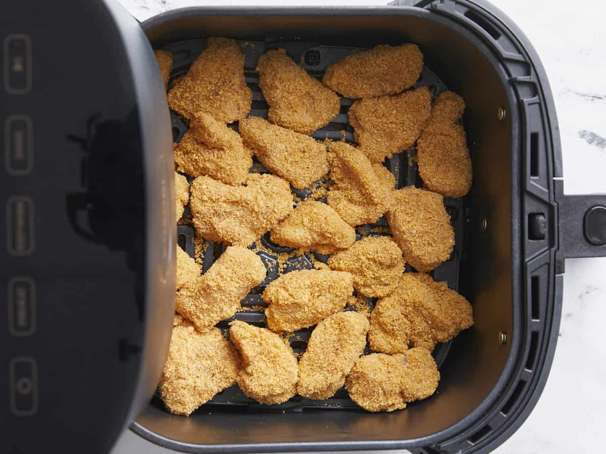 Breaded chicken nuggets added to air fryer basket.