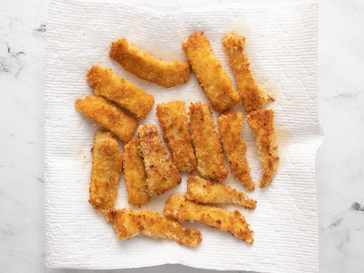 Fried fish sticks on a paper towel lined plate.