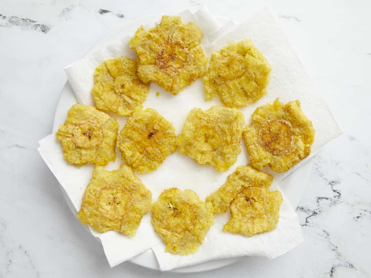 Overhead shot of fried tostones on paper towel-lined plate.