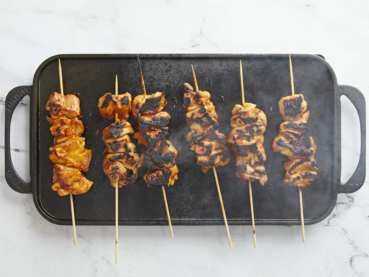 Overhead shot of Pinchos De Pollo cooking on a black grill plate.