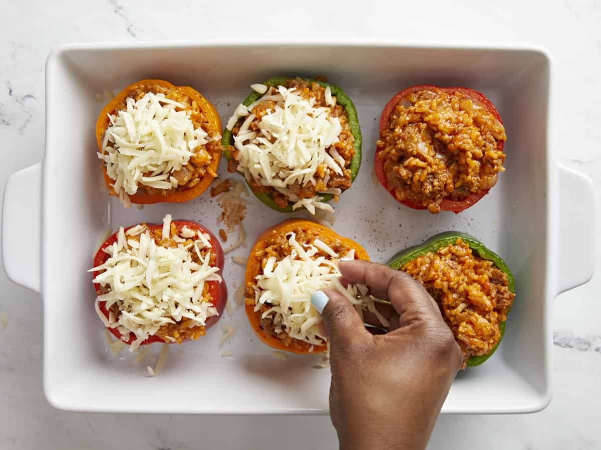 Overhead view of stuffed bell peppers with mozzarella cheese being added on top.
