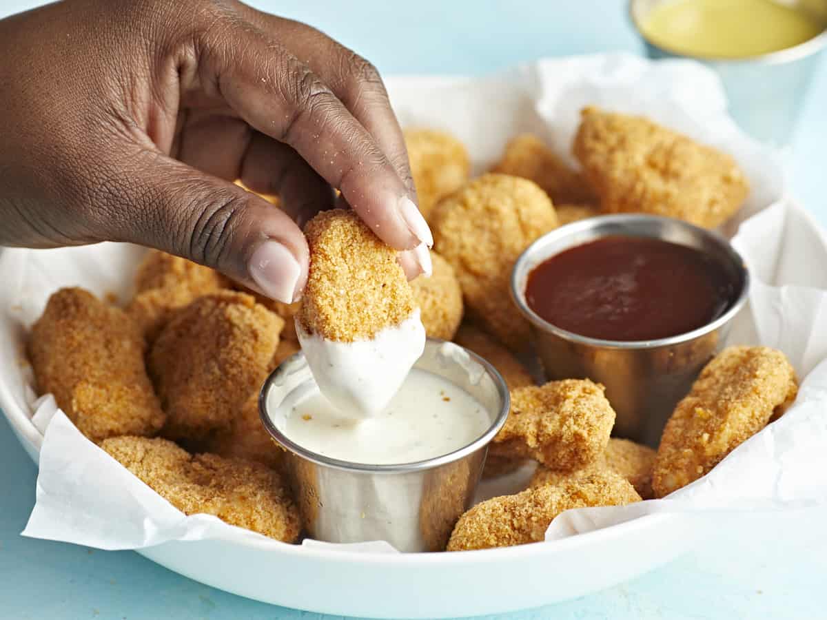 Plated air fryer chicken nuggets with one nugget being dipped in ranch dipping sauce.