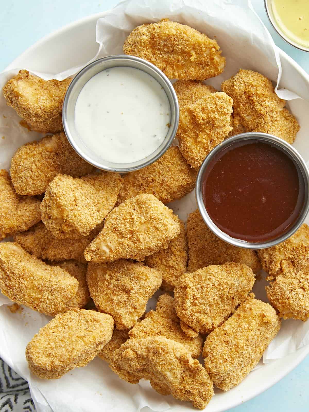 Air fryer chicken nuggets in a serving dish with BBQ and ranch dipping sauces.