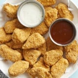Air fryer chicken nuggets plated in a serving dish with ranch and BBQ dipping sauces on the side.