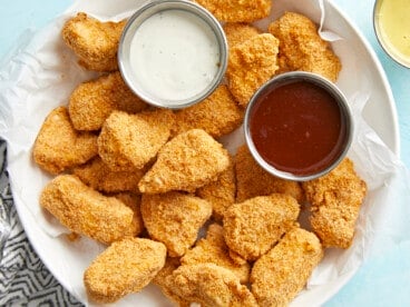 Air fryer chicken nuggets plated in a serving dish with ranch and BBQ dipping sauces on the side.