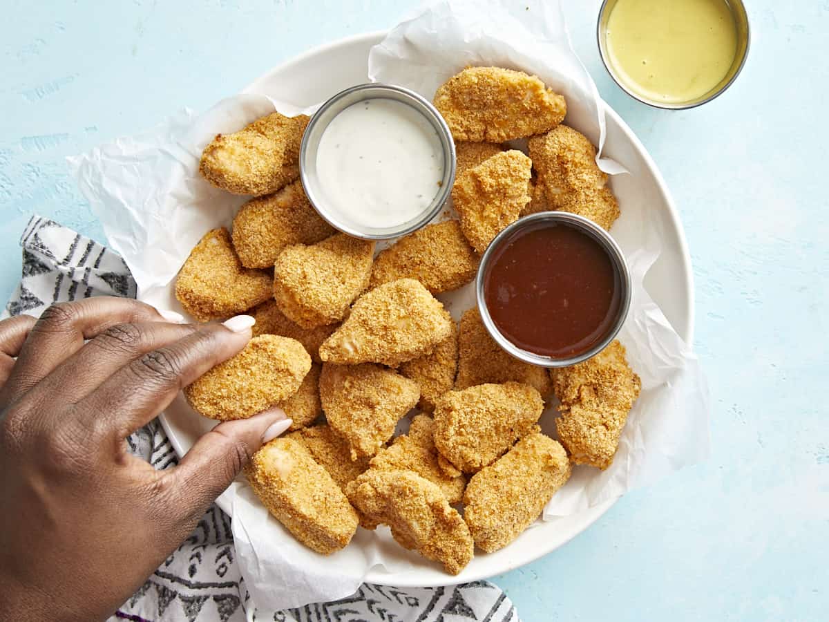 Plated air fryer chicken nuggets with one nugget being grabbed.