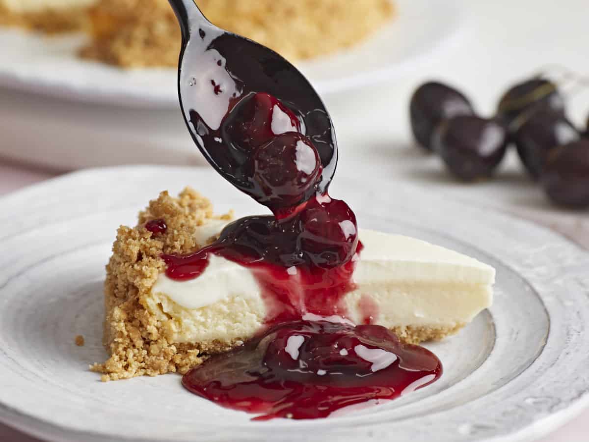 Cherry sauce being drizzled over a piece of cheesecake.