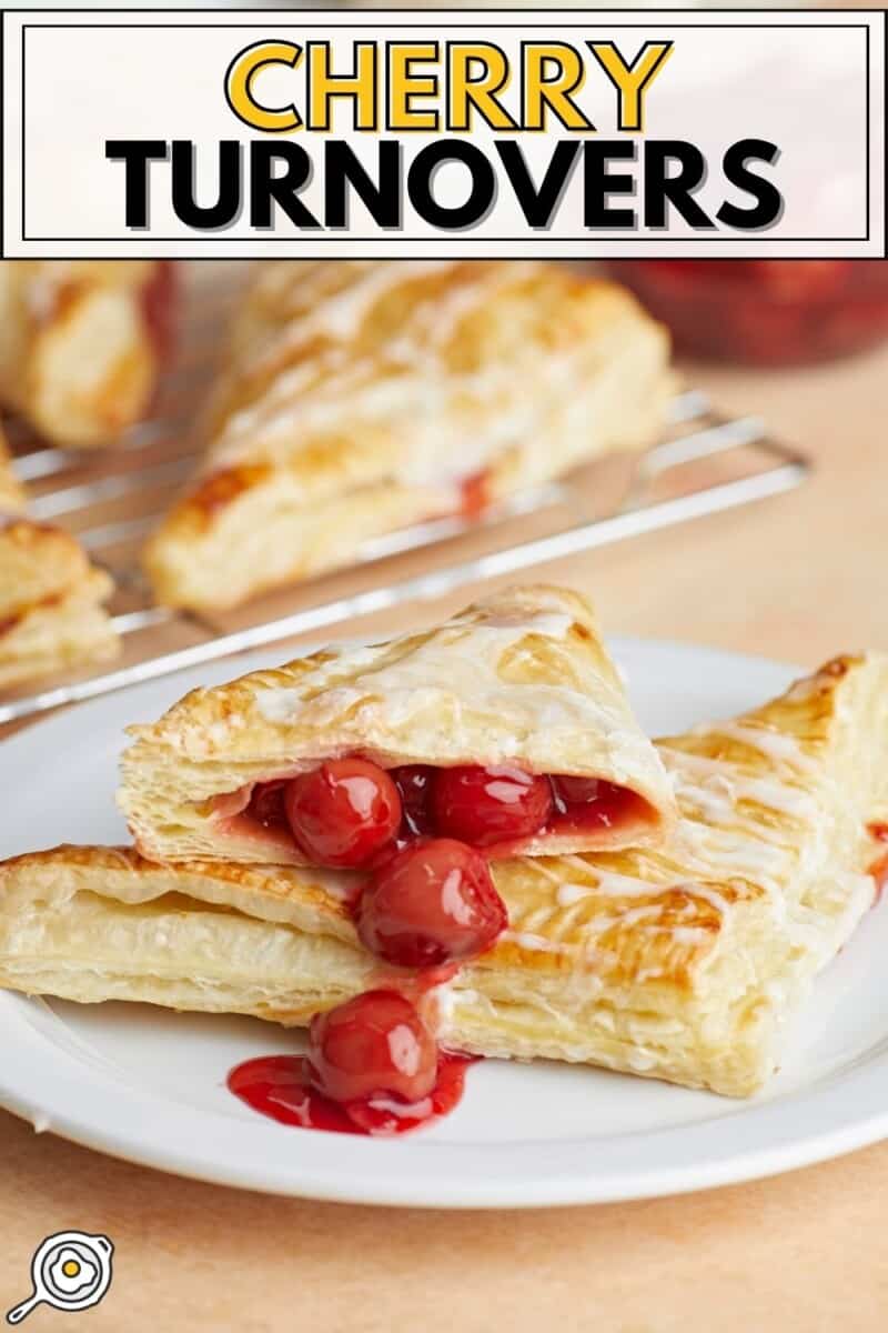 Two cherry turnovers stacked on a plate, one cut in half with the filling spilling out.