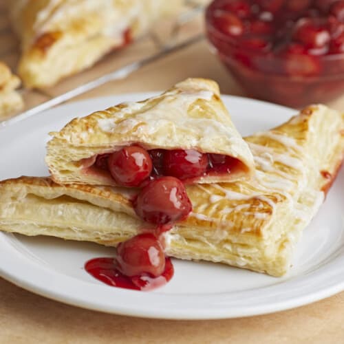 Two cherry turnovers stacked on a plate, one cut in half with filling spilling out.