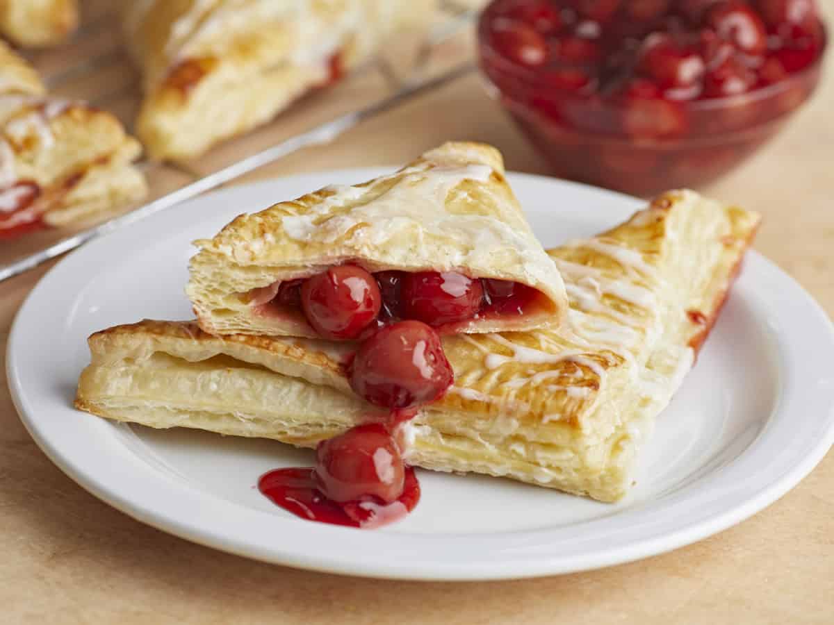 Two cherry turnovers stacked on a plate, one cut in half with the filling spilling out.