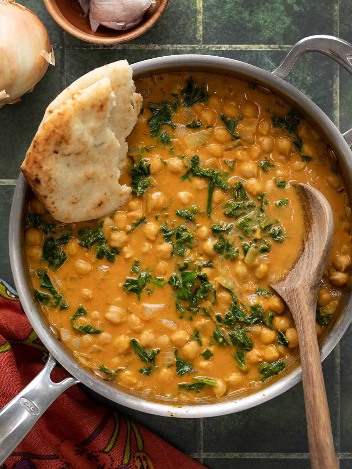 Finished skillet full of coconut curry chickpeas with naan and a wooden spoon.