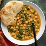 Overhead view of a bowl full of coconut curry chickpeas with a piece of naan.