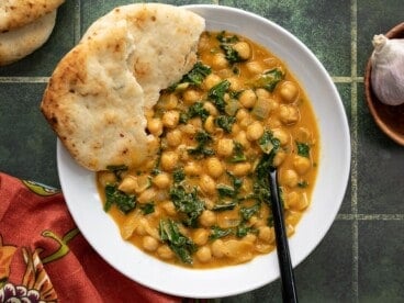 Overhead view of a bowl full of coconut curry chickpeas with a piece of naan.