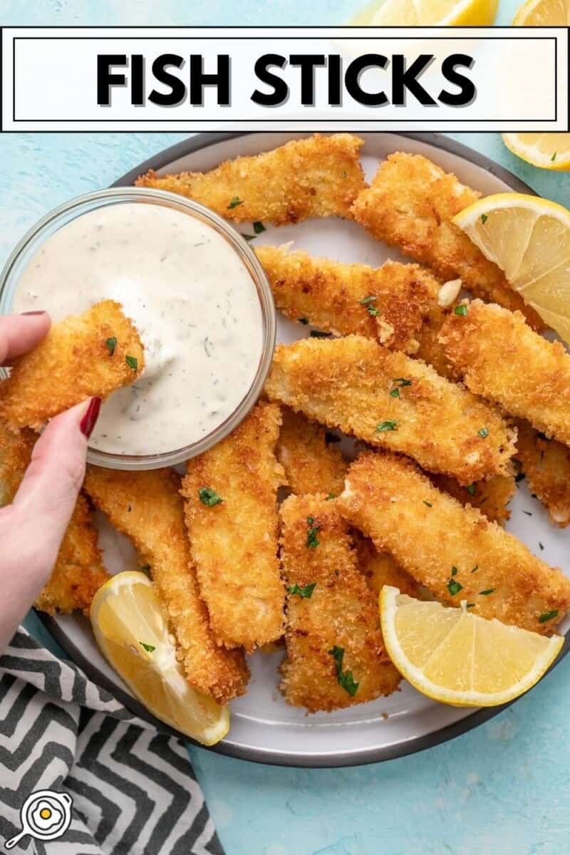 A hand dipping a fish stick into a bowl of tartar sauce on a plate full of fish sticks.