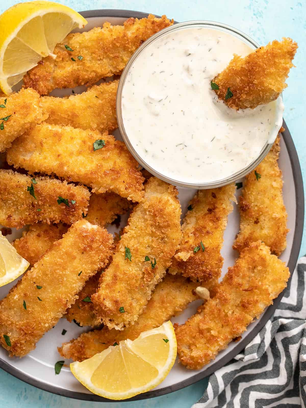 Close up overhead view of a plate full of fish sticks with one dipped into tartar sauce.