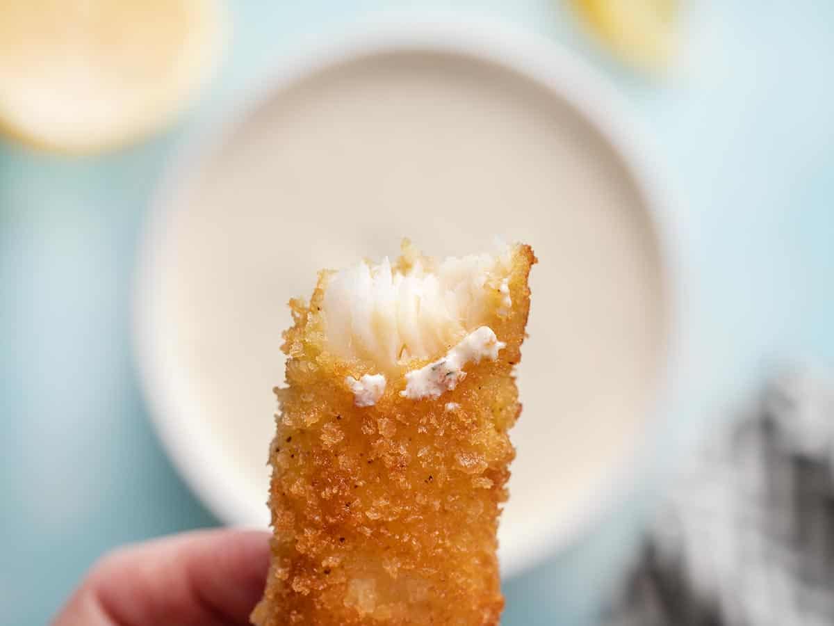 Close up of a fish stick with a bite taken out, showing the flakey interior.