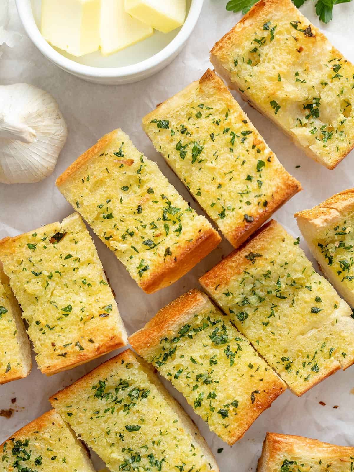 Slices of homemade garlic bread on a surface next to a bowl of butter.