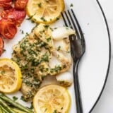 Garlic butter baked cod on a plate with roasted tomatoes and asparagus.