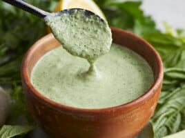 Side shot of Green Goddess Dressing in a wood bowl with a black spoon drizzling some in.