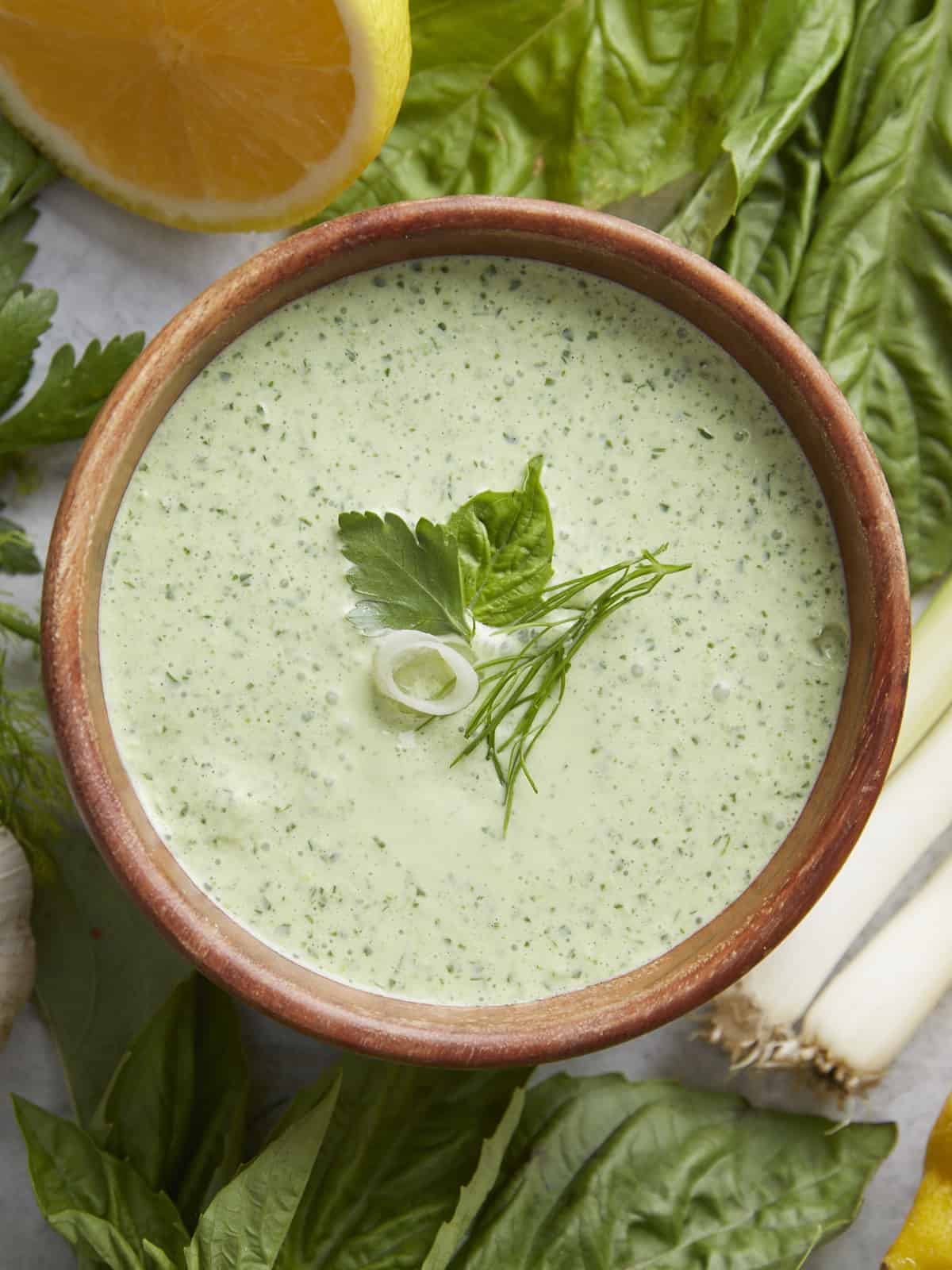 Overhead shot of Green Goddess Dressing in a wood bowl garnished with herbs.
