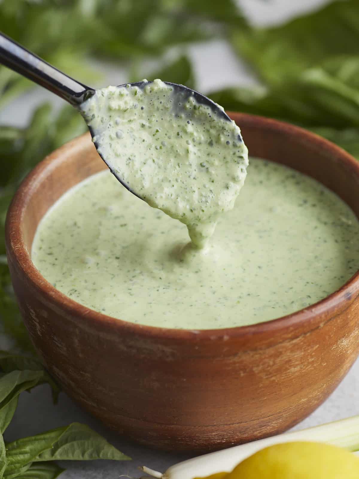 Side shot of Green Goddess Dressing in a wood bowl with a black spoon drizzling some in.