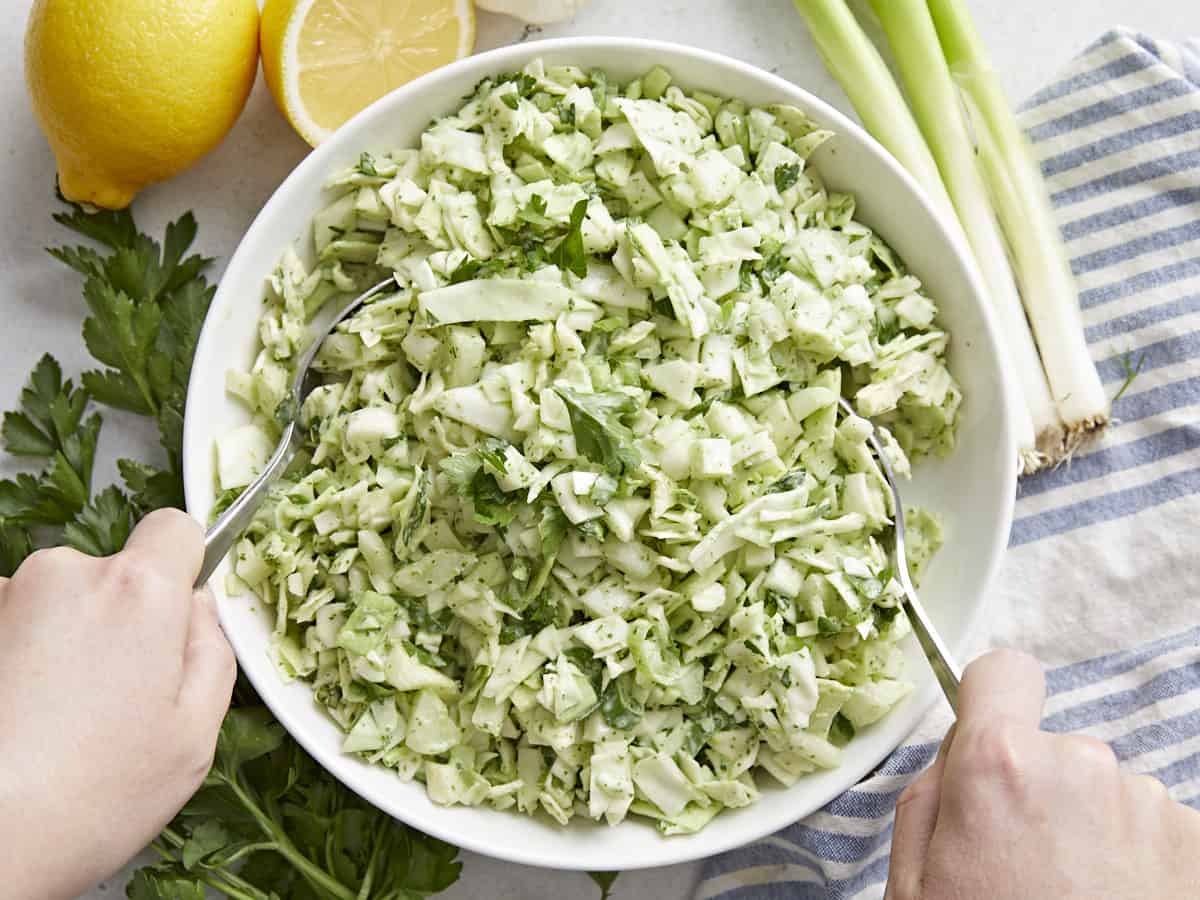 Overhead shot of Green Goddess Salad being tossed in a white bowl.