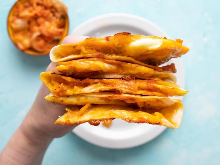 A hand holding a stack of kimchi quesadillas showing the cheese and filling.