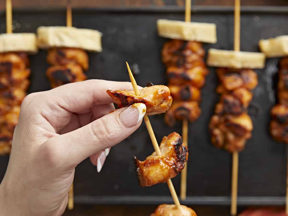 Over head shot of hand lifting Pinchos de Pollo on a black grill plate.