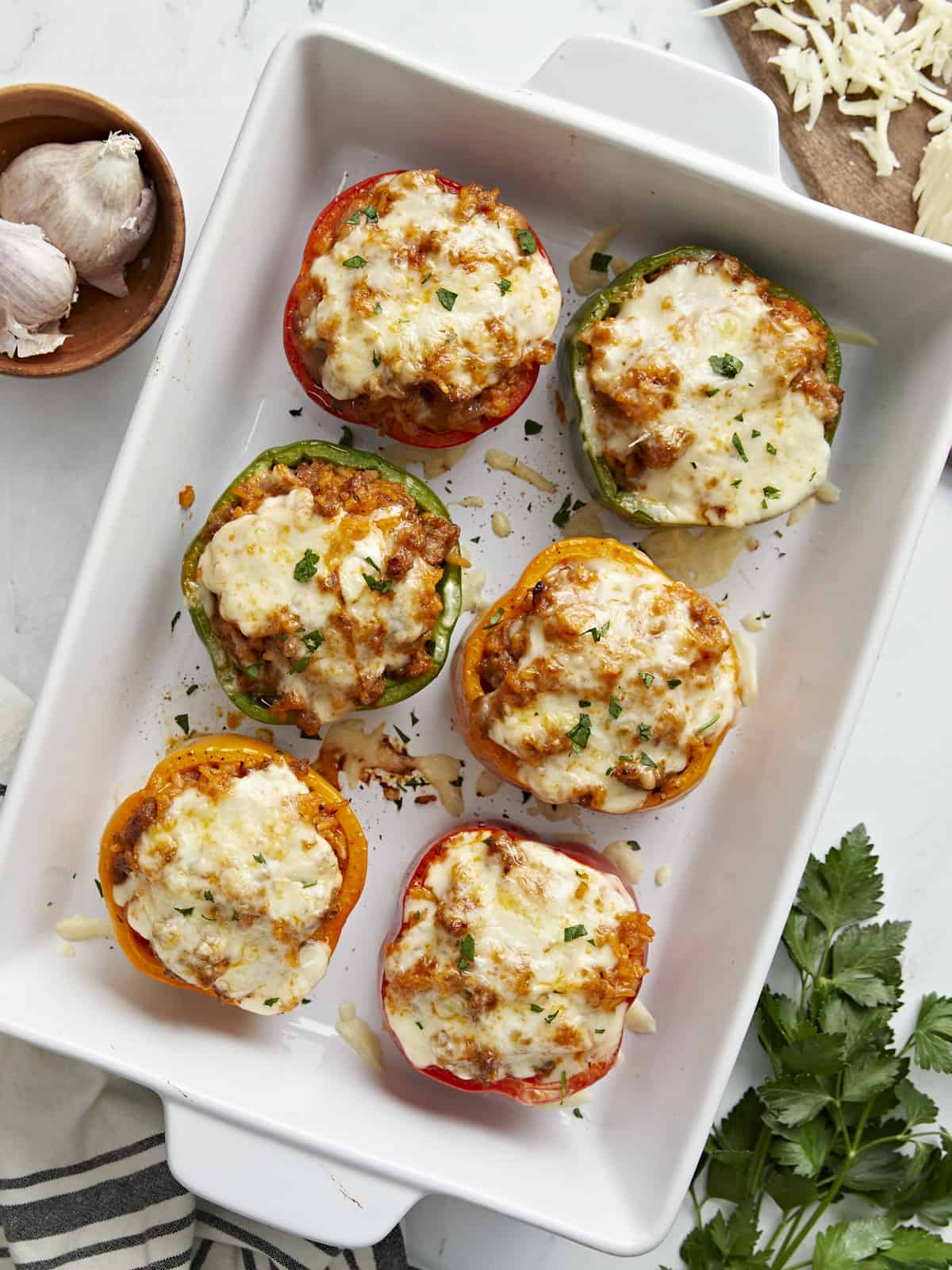 Overhead shot of stuffed bell peppers topped with mozzarella cheese and fresh parsley. Served in a white casserole dish.