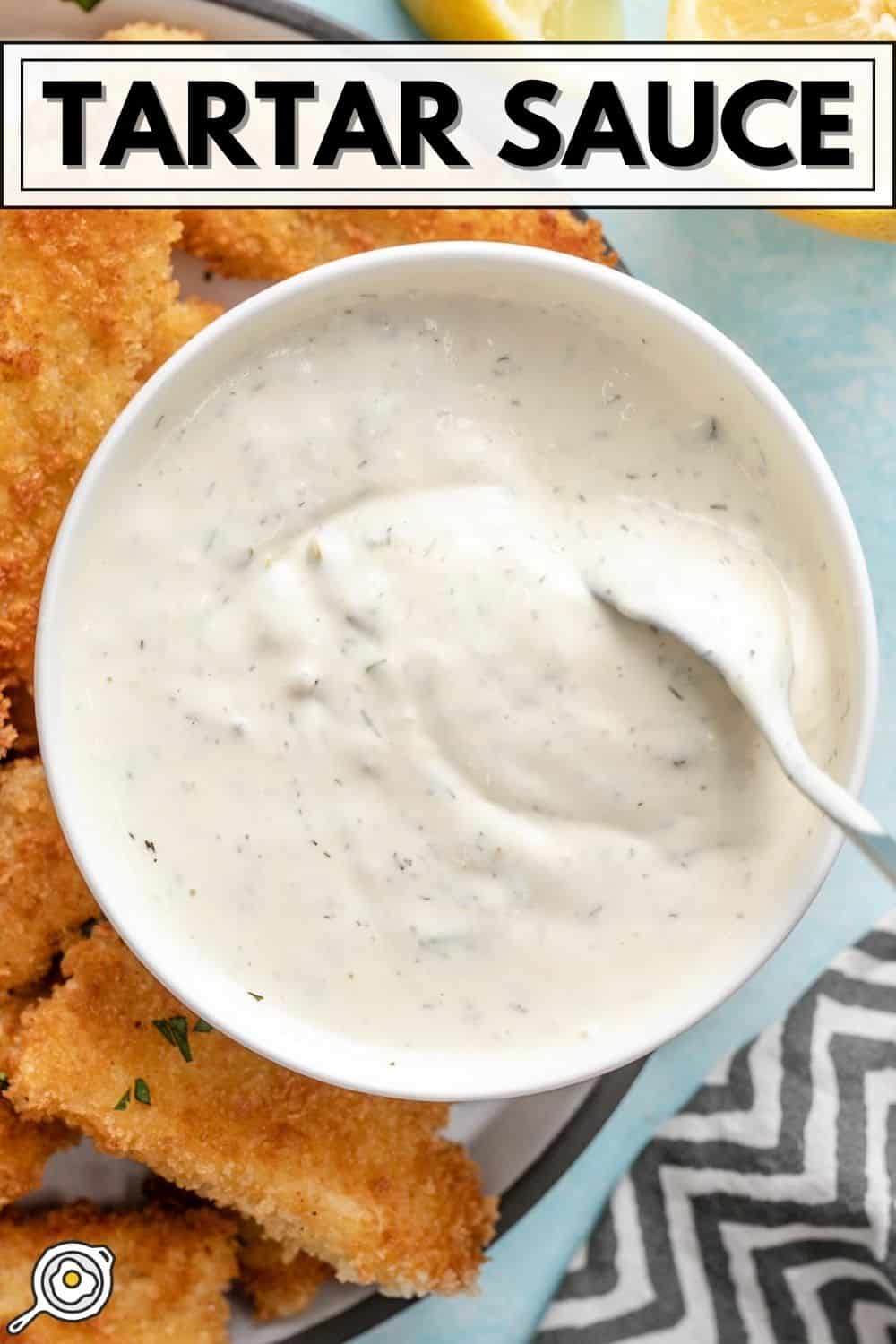 Overhead view of a bowl of tartar sauce being stirred with a spoon.