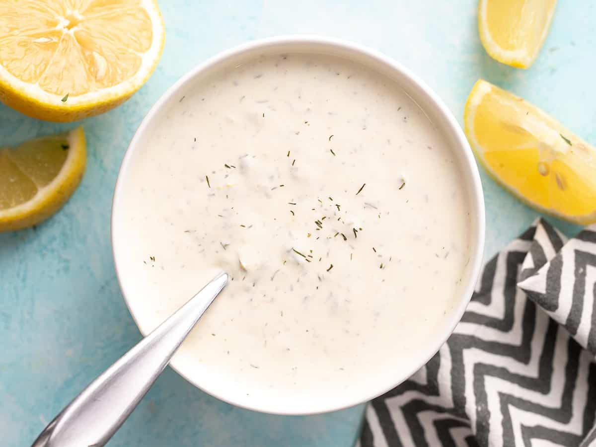 Overhead view of a bowl full of tartar sauce with lemons on the side.