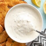 Overhead view of a bowl of tartar sauce with a spoon, on a plate of fish sticks.