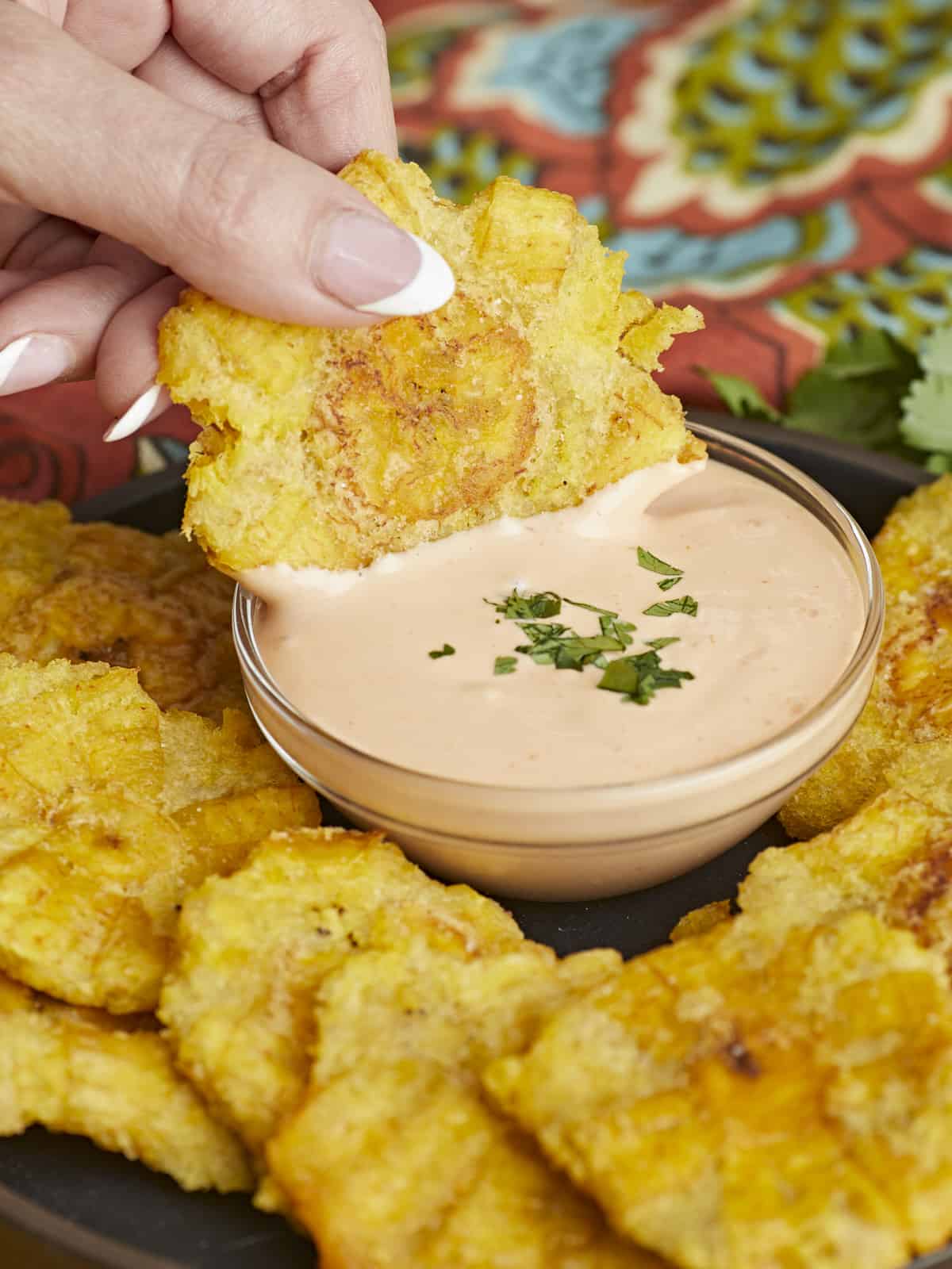 Side shot of hand dipping a fried toston in mayo-ketchup sauce.