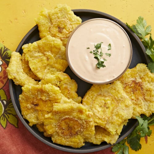 Overhead shot of fried tostones in a black bowl with mayo-ketchup sauce in the middle of the bowl.