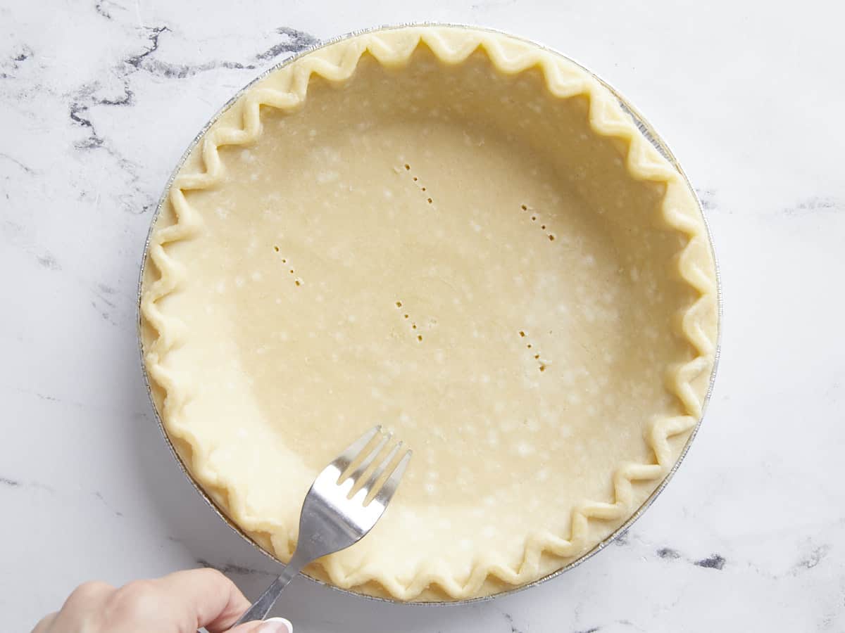 Pie crust being pricked with a fork. 