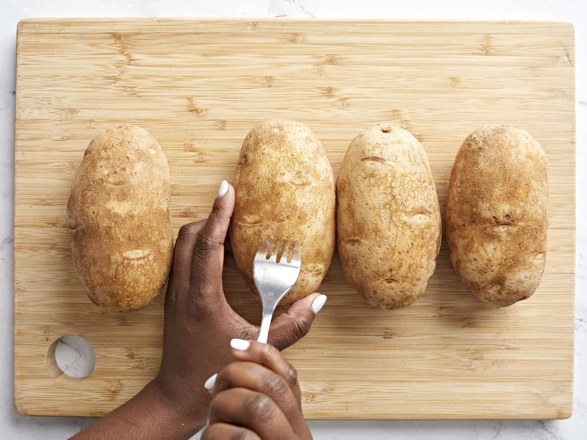 4 russet potatoes being pierced with a fork.