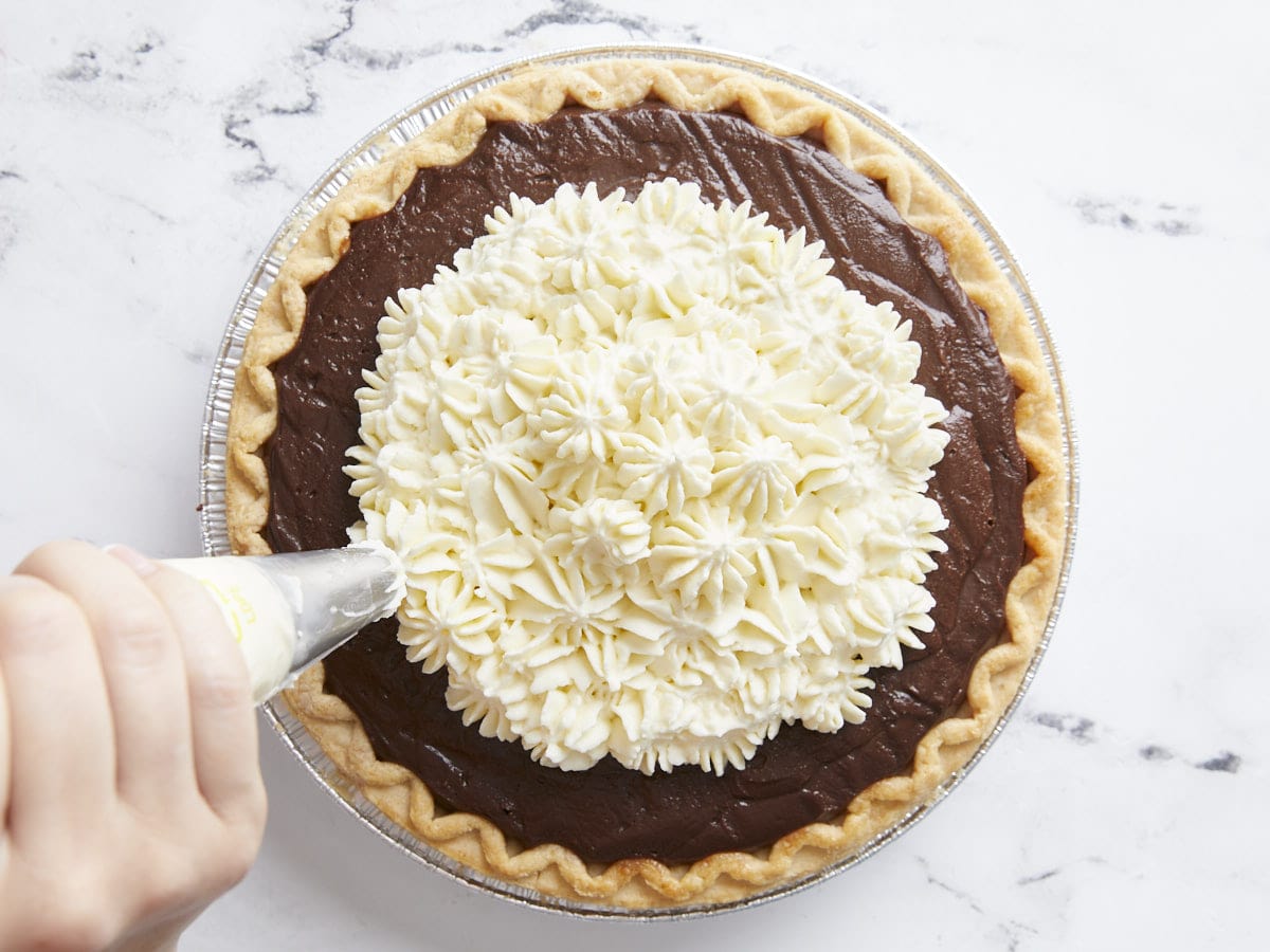Whipped cream being piped onto the chocolate cream pie. 