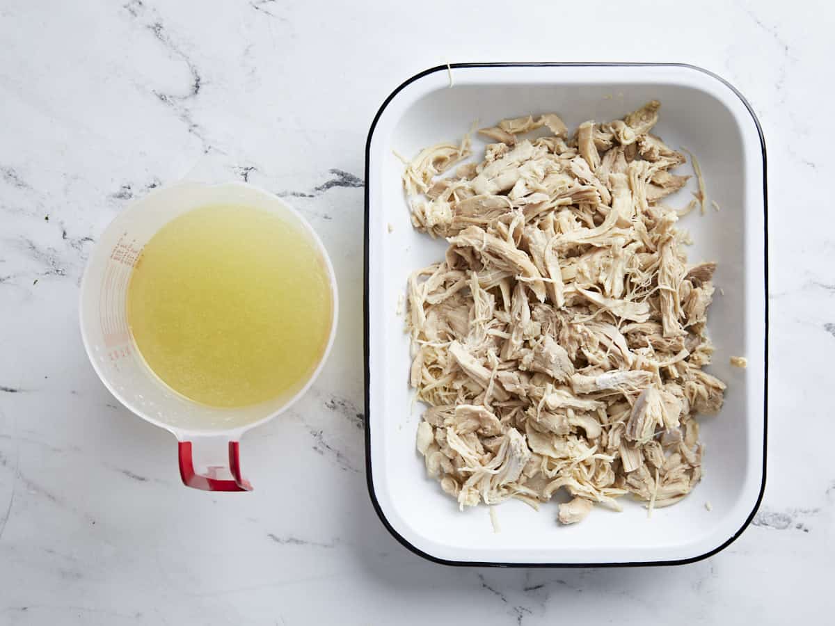 Shredded chicken in a dish, a measuring cup with broth on the side.