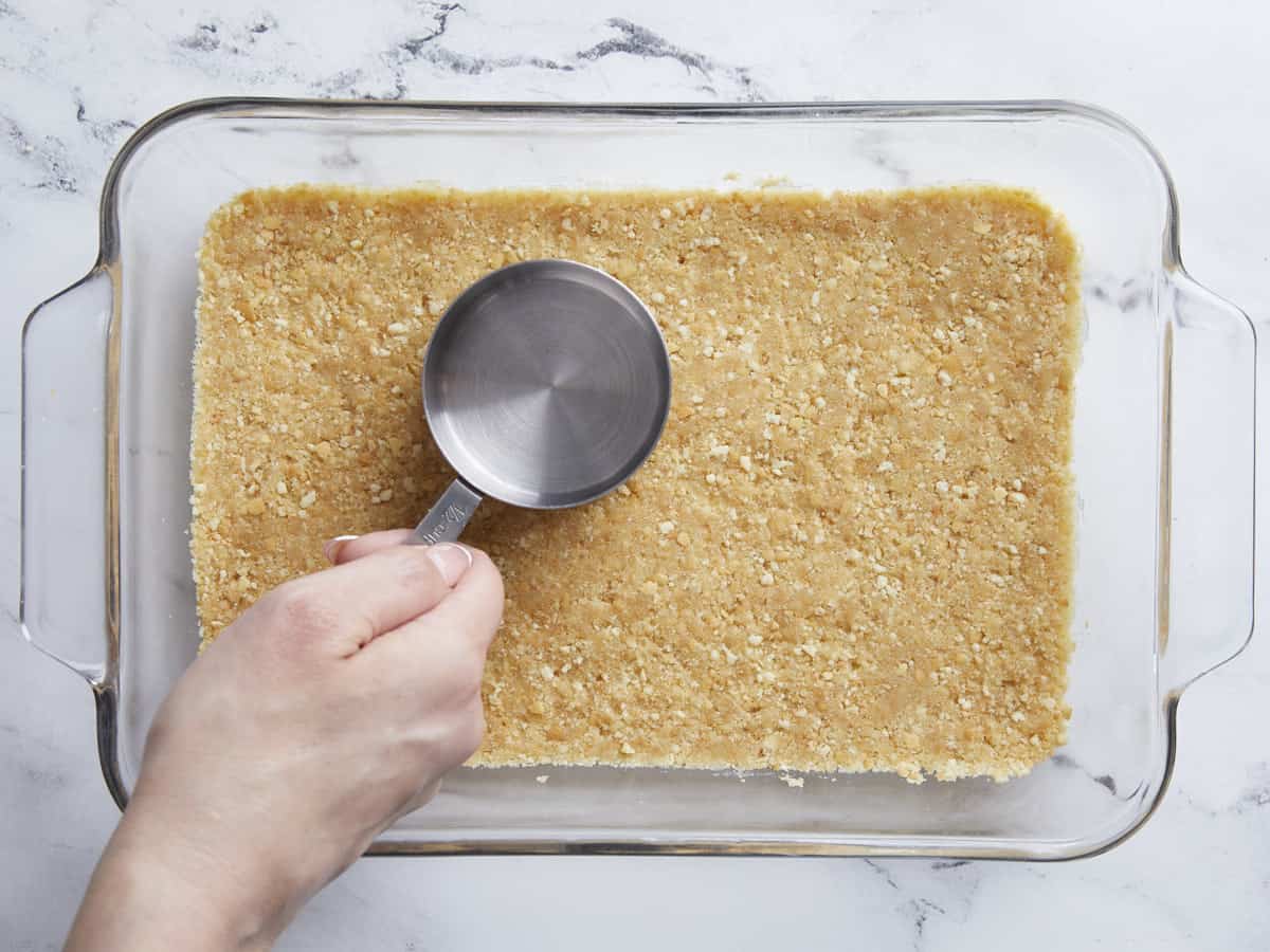 Vanilla wafer crust being pressed into a baking dish. 