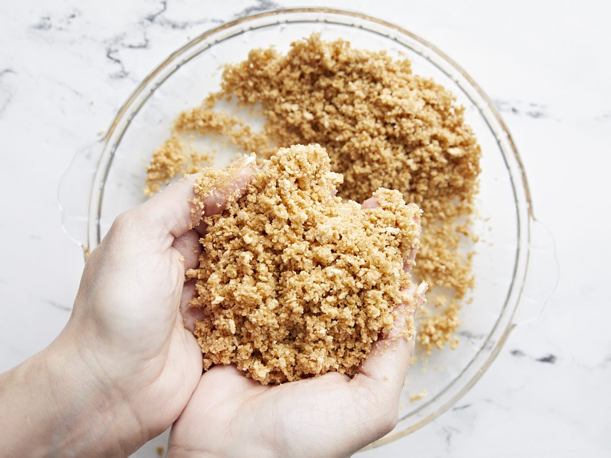 Graham cracker and butter mixture held in a pair of hands.