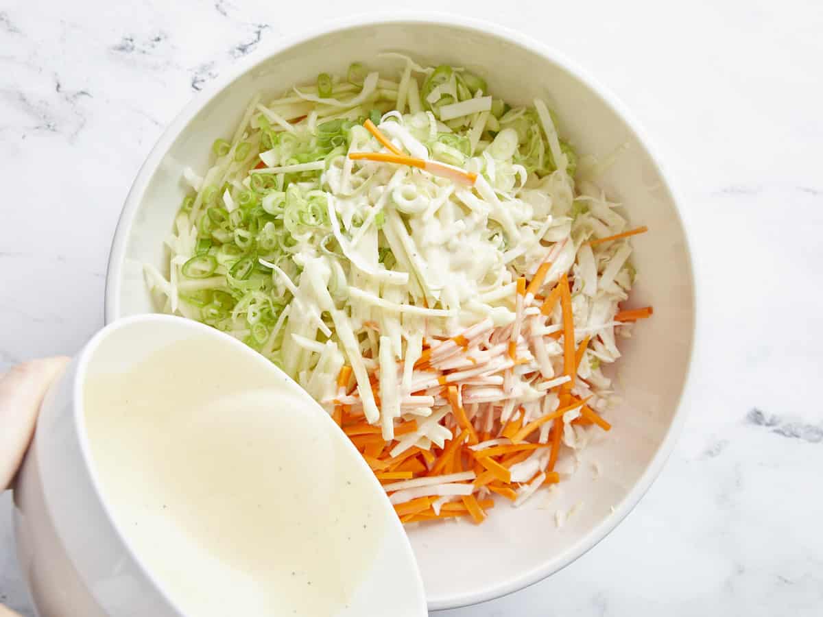 Dressing being poured over the bowl of shredded vegetables.