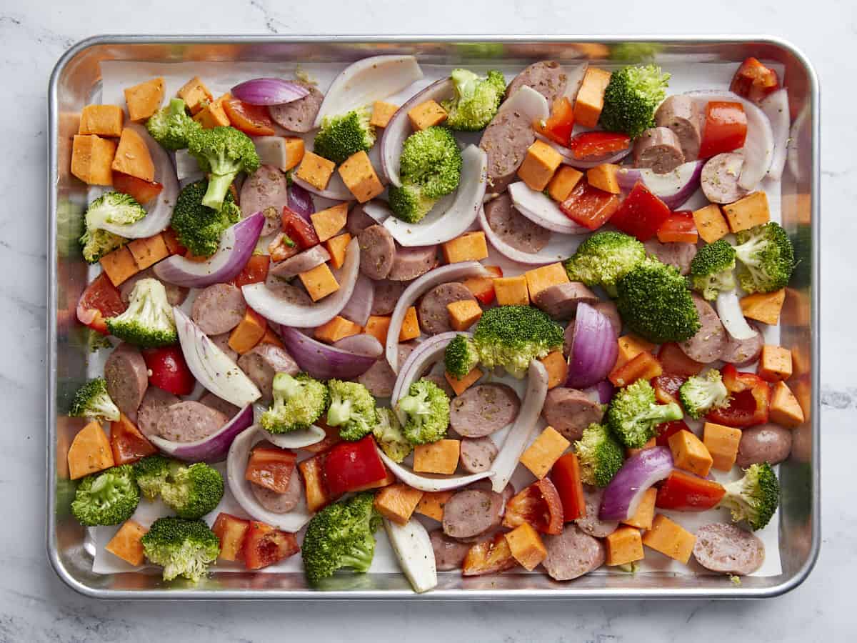 Seasoned chicken sausage and vegetables spread out on a baking sheet.