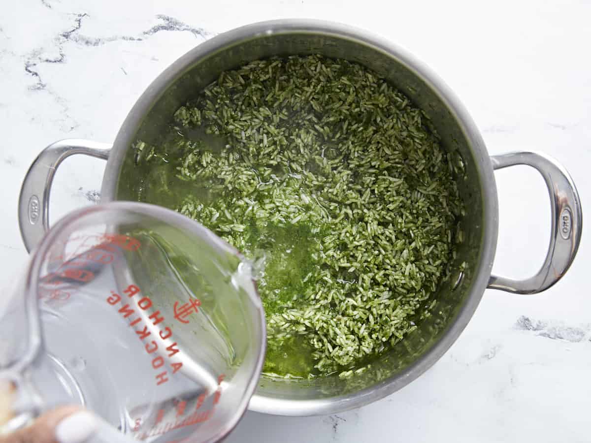 Boiling water being added to rice and green vegetable mixture inside the pot