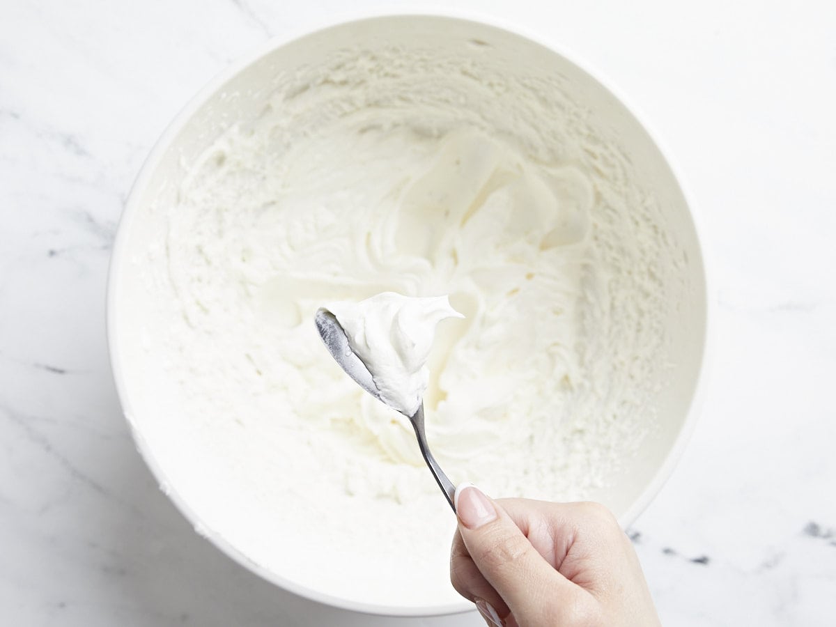 Heavy cream whipped to stiff peaks in a white bowl.