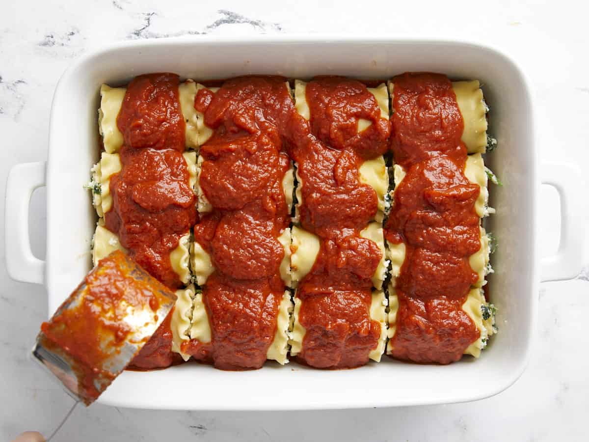 Sauce being poured over the lasagna roll ups in the baking dish.